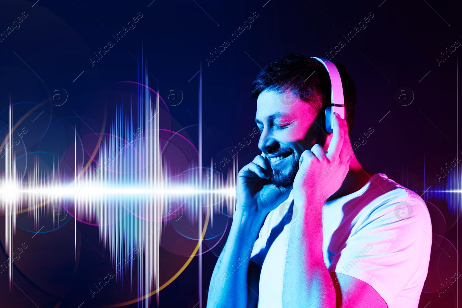 Image of Man with headphones listening to music in neon lights against dark blue background. Sound waves behind him