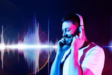 Image of Man with headphones listening to music in neon lights against dark blue background. Sound waves behind him