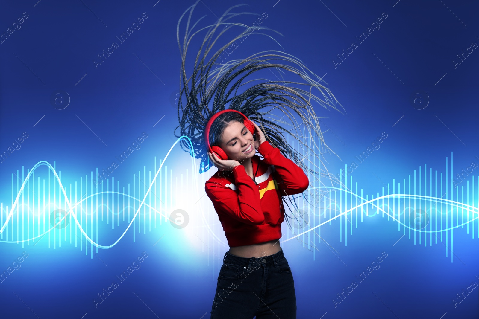 Image of Beautiful woman with headphones listening to music and dancing on blue background. Sound waves behind her