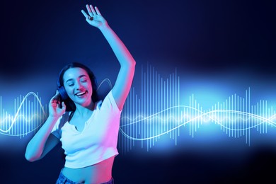 Image of Happy woman with headphones listening music and dancing in neon lights against dark blue background. Sound waves behind her