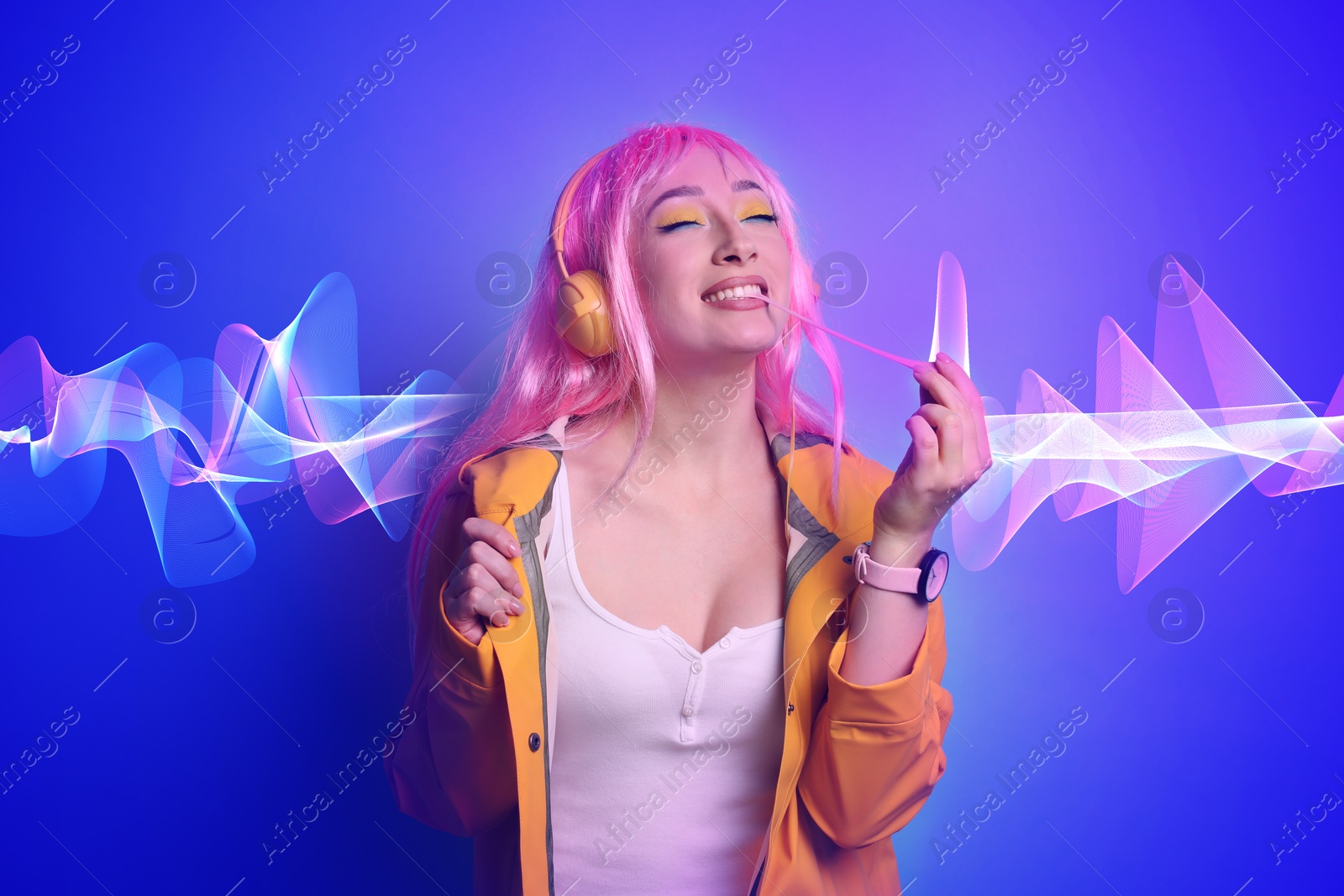 Image of Fashionable young woman in pink wig with headphones listening to music on blue background. Sound waves behind her