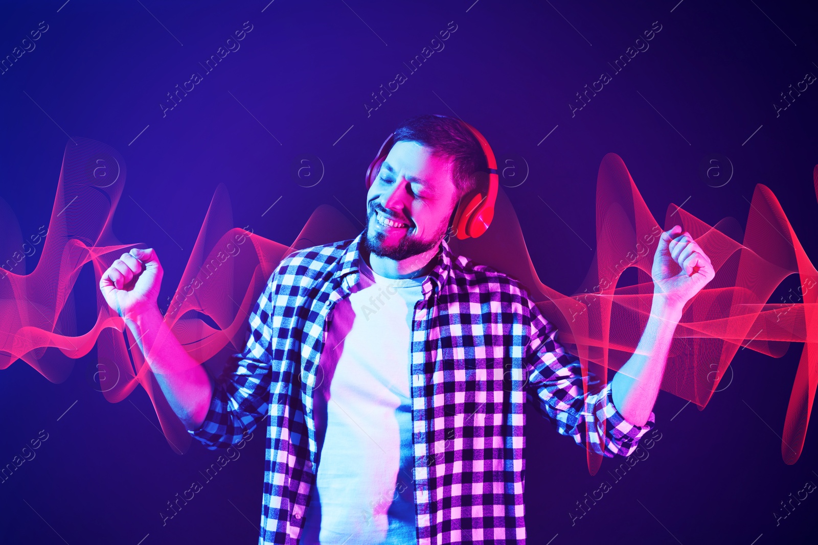 Image of Happy man with headphones listening to music in neon lights against dark blue background. Sound waves behind him