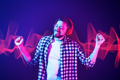 Image of Happy man with headphones listening to music in neon lights against dark blue background. Sound waves behind him