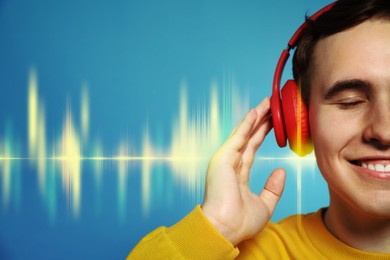 Handsome young man with headphones listening to music on light blue background, closeup. Sound waves