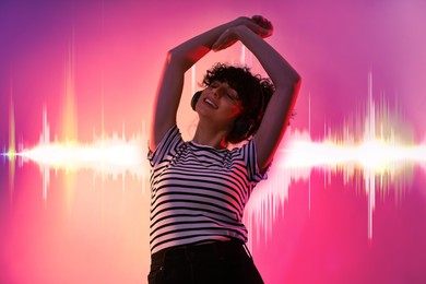 Young woman with headphones listening to music and dancing on color gradient background. Sound waves behind her