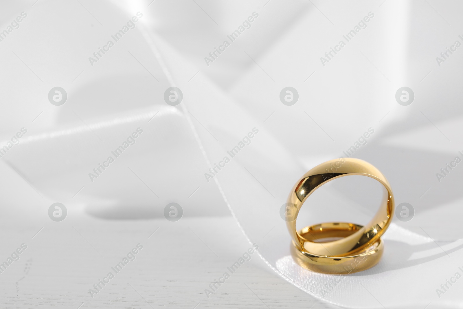 Photo of Beautiful golden wedding rings and white ribbon on light wooden background