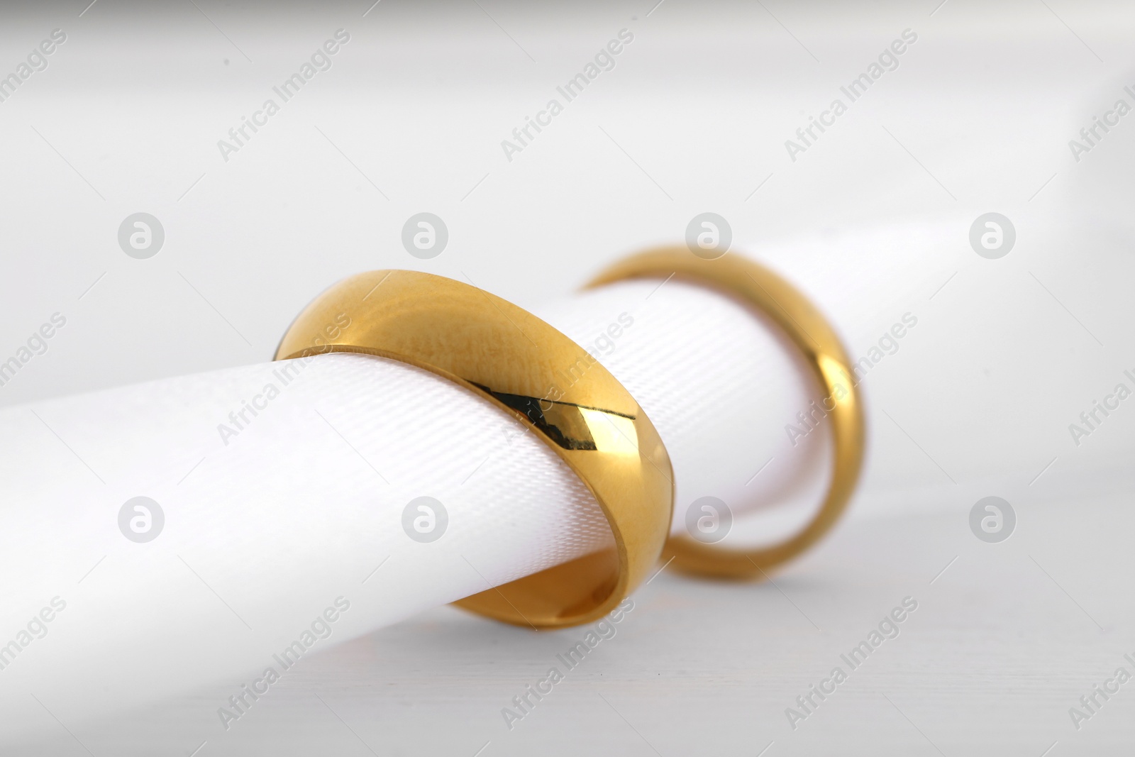 Photo of Beautiful golden wedding rings and white ribbon on light wooden background, closeup