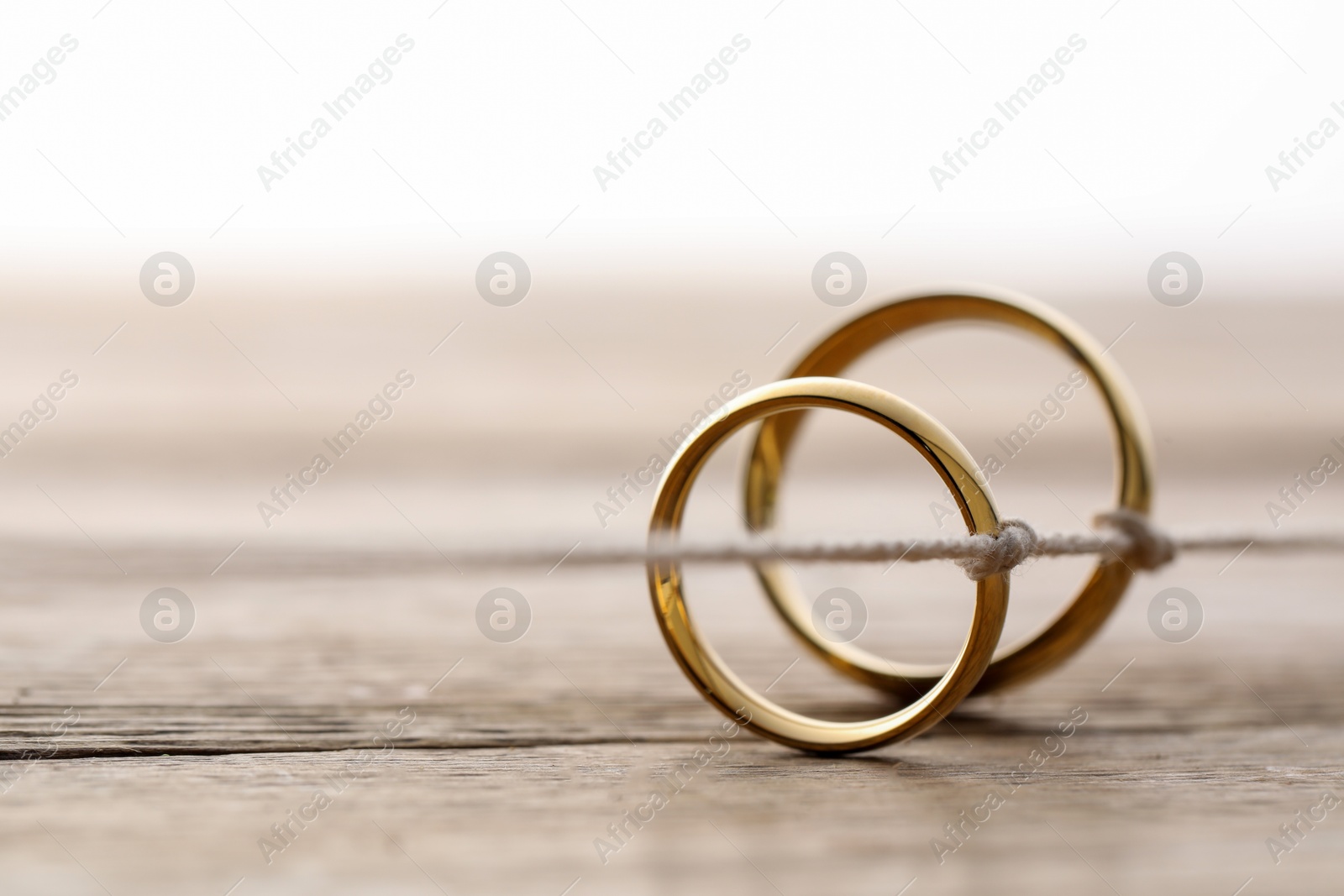 Photo of Beautiful golden wedding rings tied with thread on wooden background, selective focus