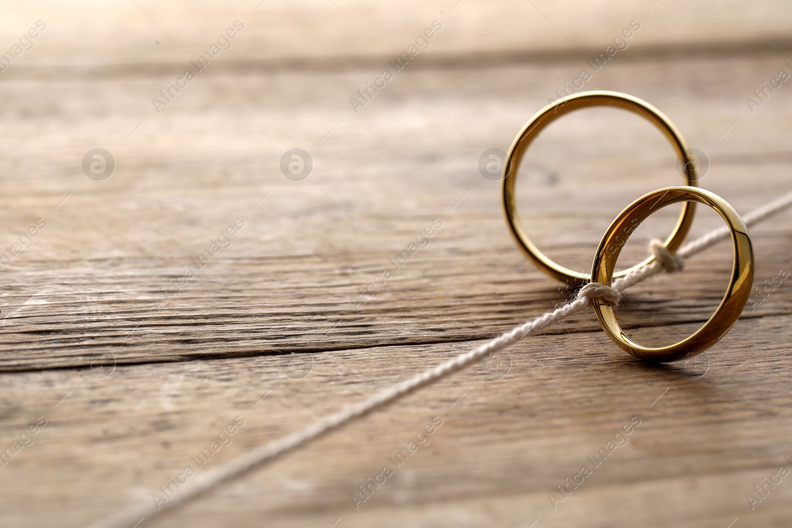 Photo of Beautiful golden wedding rings tied with thread on wooden background, space for text