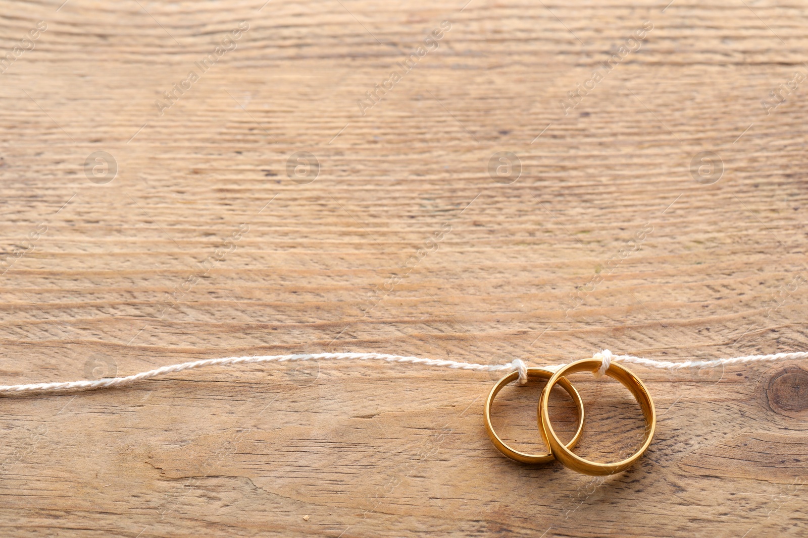 Photo of Beautiful golden wedding rings tied with thread on wooden background, above view. Space for text