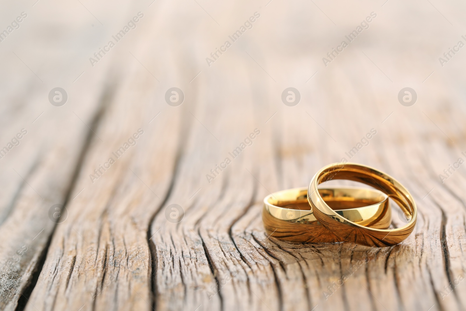 Photo of Beautiful golden wedding rings on wooden background, space for text