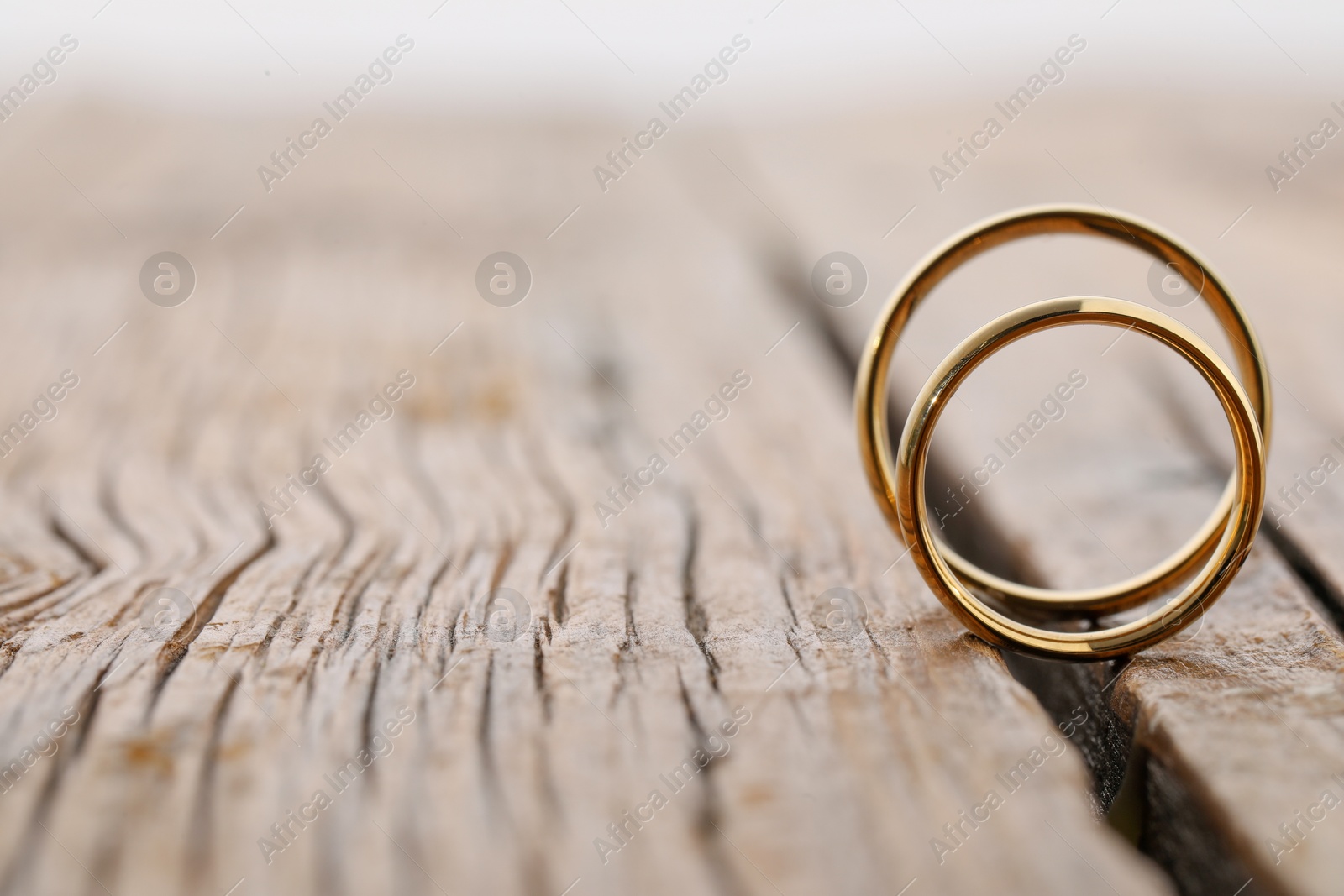 Photo of Beautiful golden wedding rings on wooden background, space for text