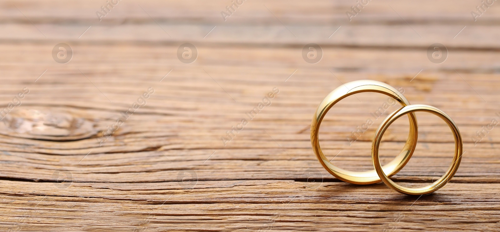 Photo of Beautiful golden wedding rings on wooden background, space for text