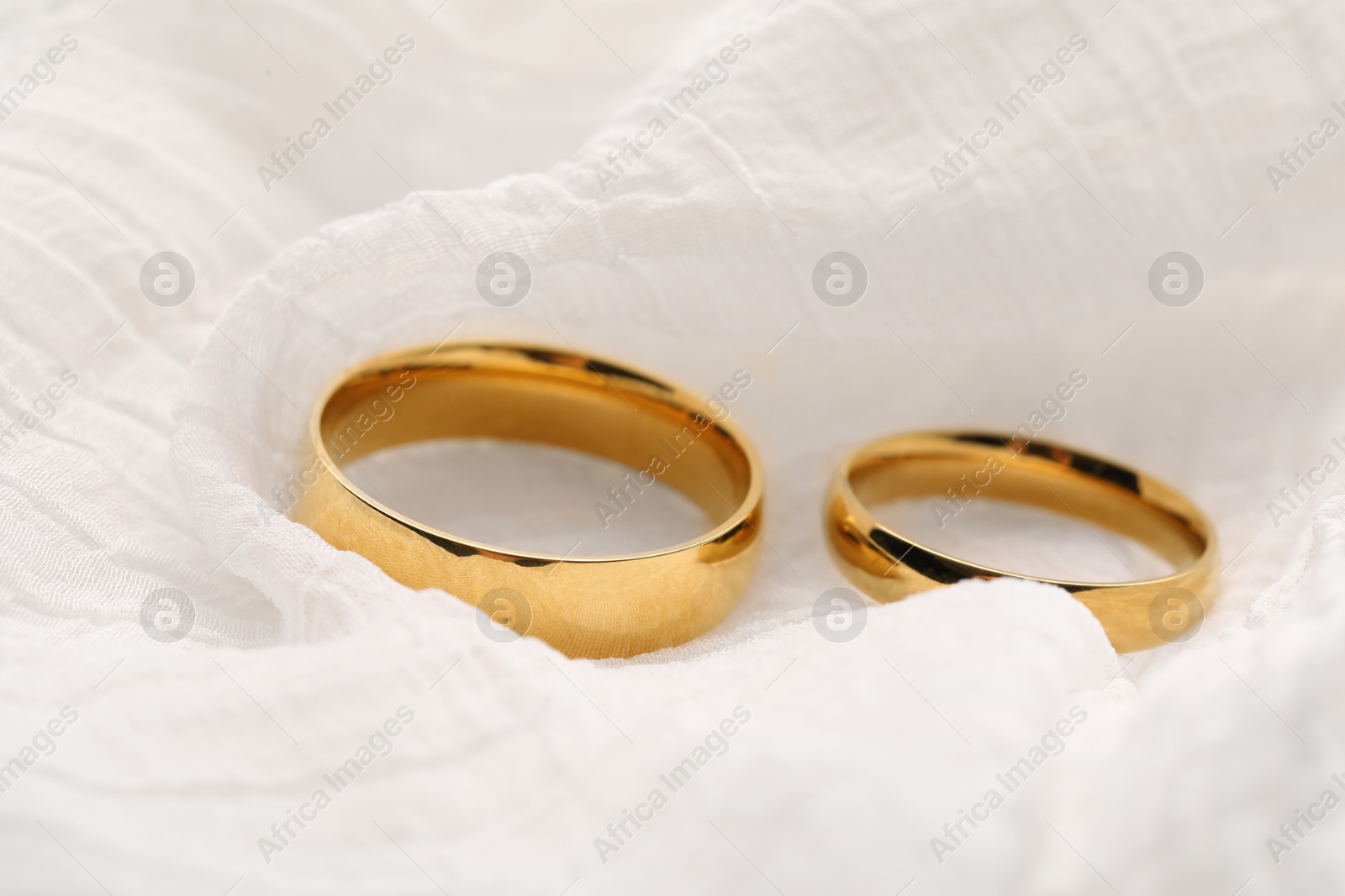 Photo of Beautiful golden wedding rings on white fabric, closeup