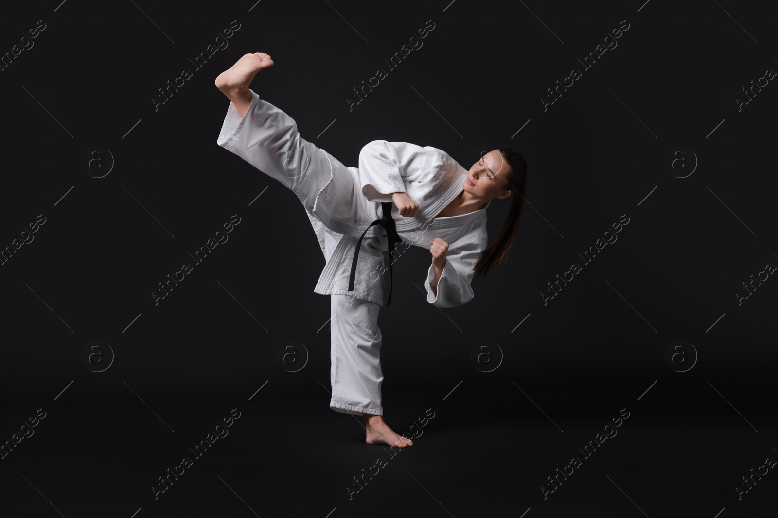 Photo of Young woman in kimono practicing karate on black background