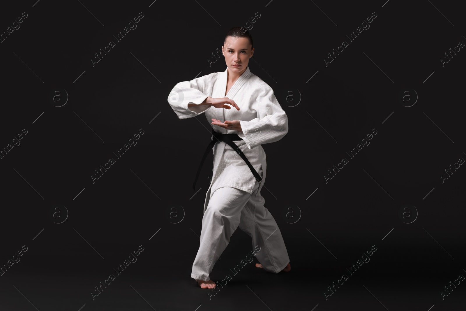 Photo of Young woman in kimono practicing karate on black background