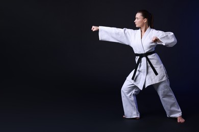 Photo of Young woman in kimono practicing karate on dark background, space for text