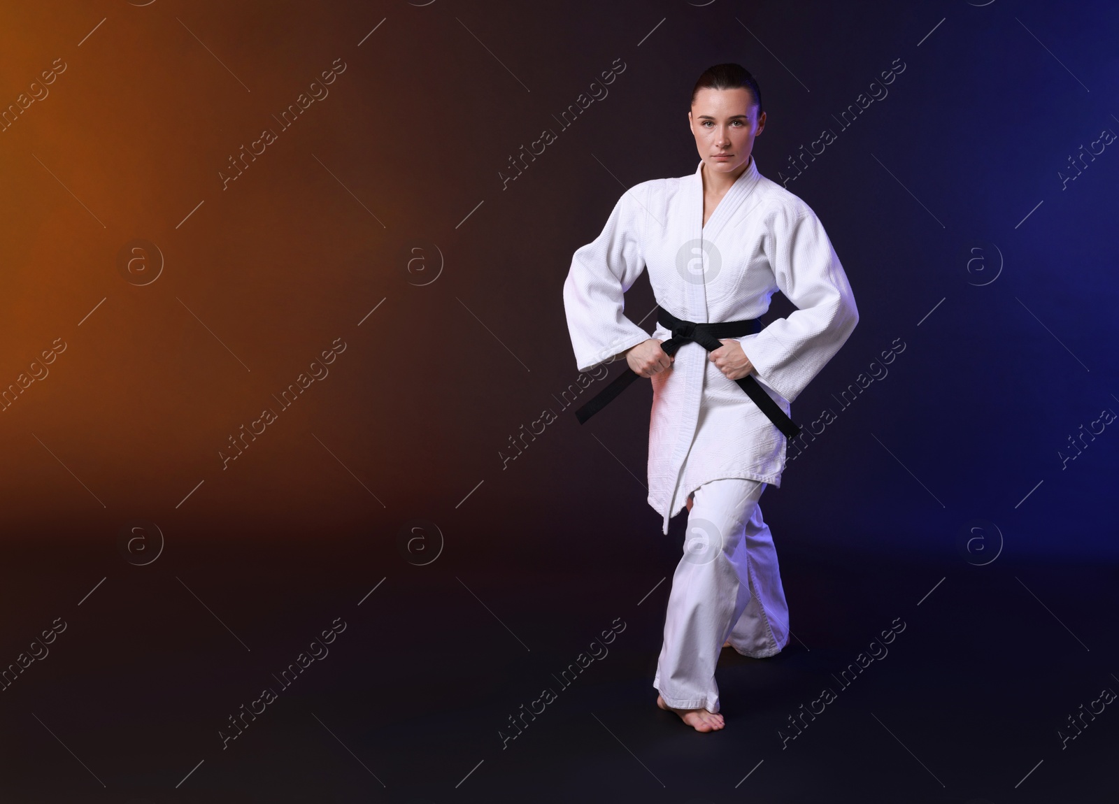 Photo of Young woman in kimono practicing karate on dark background, space for text