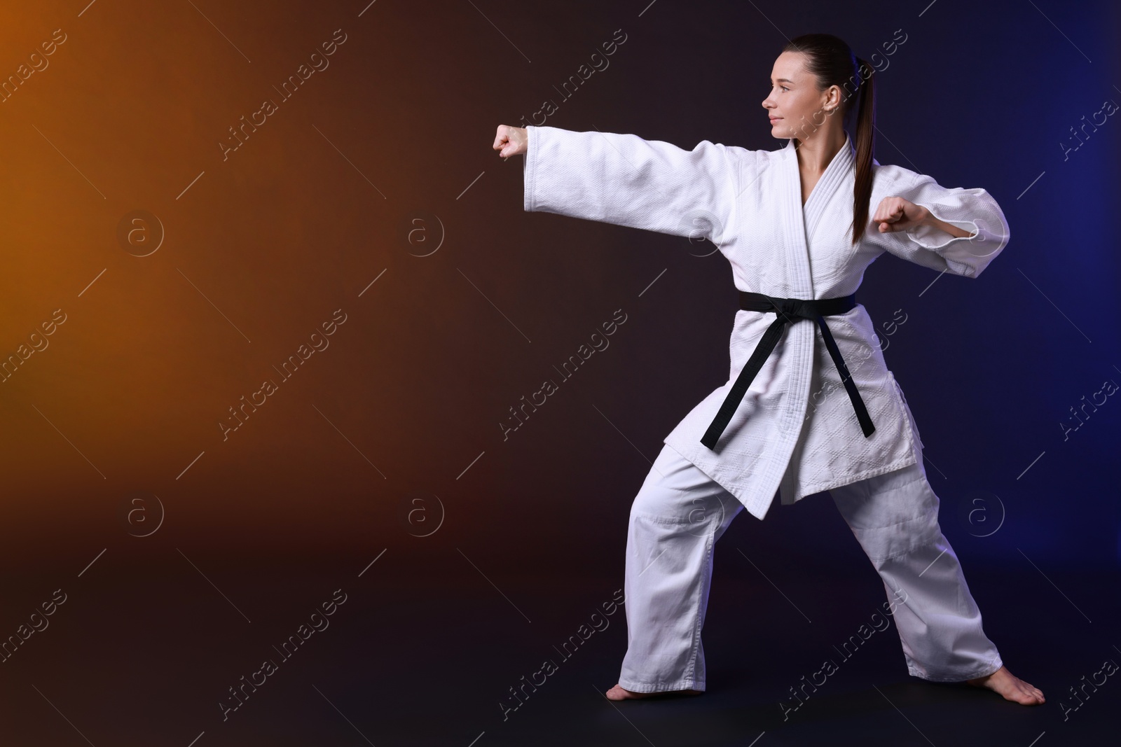 Photo of Young woman in kimono practicing karate on dark background, space for text