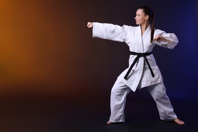 Photo of Young woman in kimono practicing karate on dark background, space for text