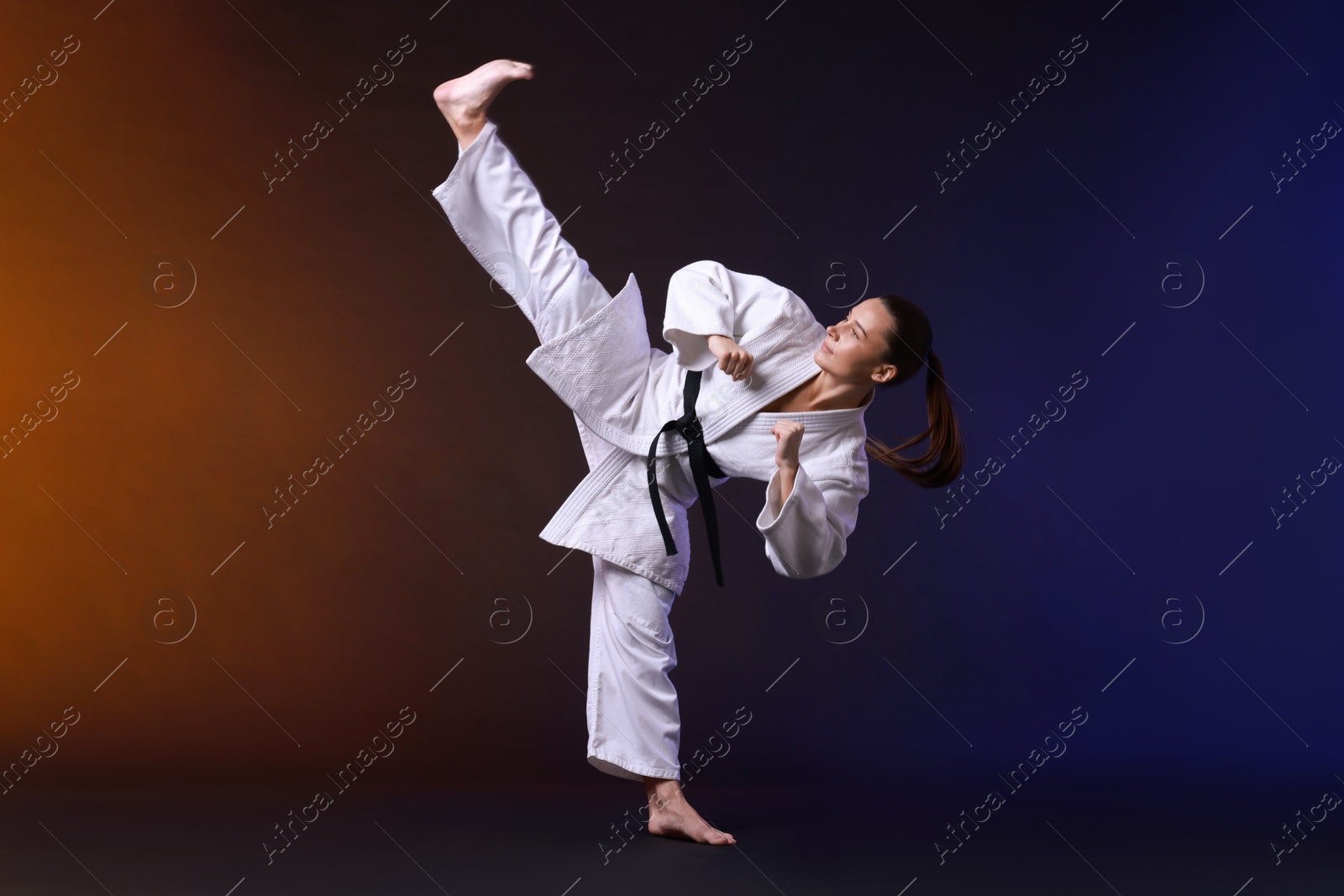 Photo of Young woman in kimono practicing karate on dark background