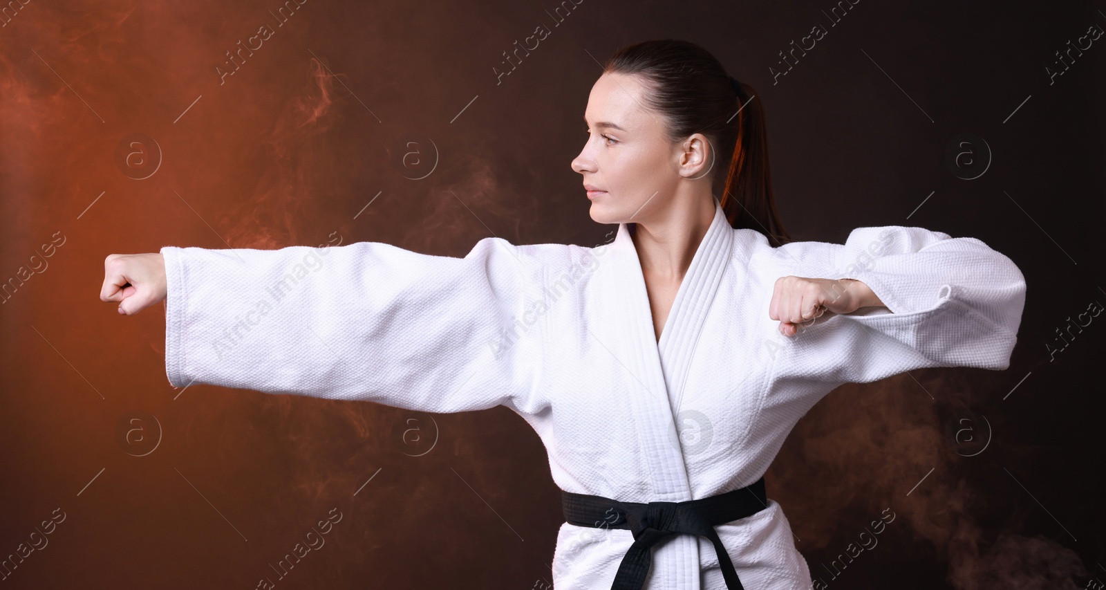 Photo of Young woman in kimono practicing karate on dark background