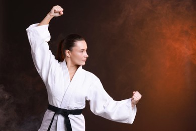 Photo of Young woman in kimono practicing karate on dark background, space for text