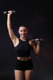 Photo of Woman exercising with dumbbells in smoke on dark background