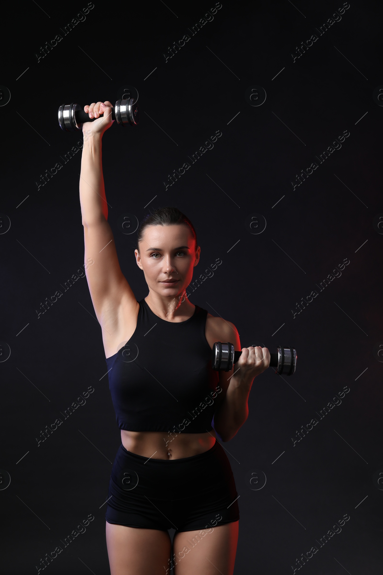 Photo of Woman exercising with dumbbells in smoke on dark background