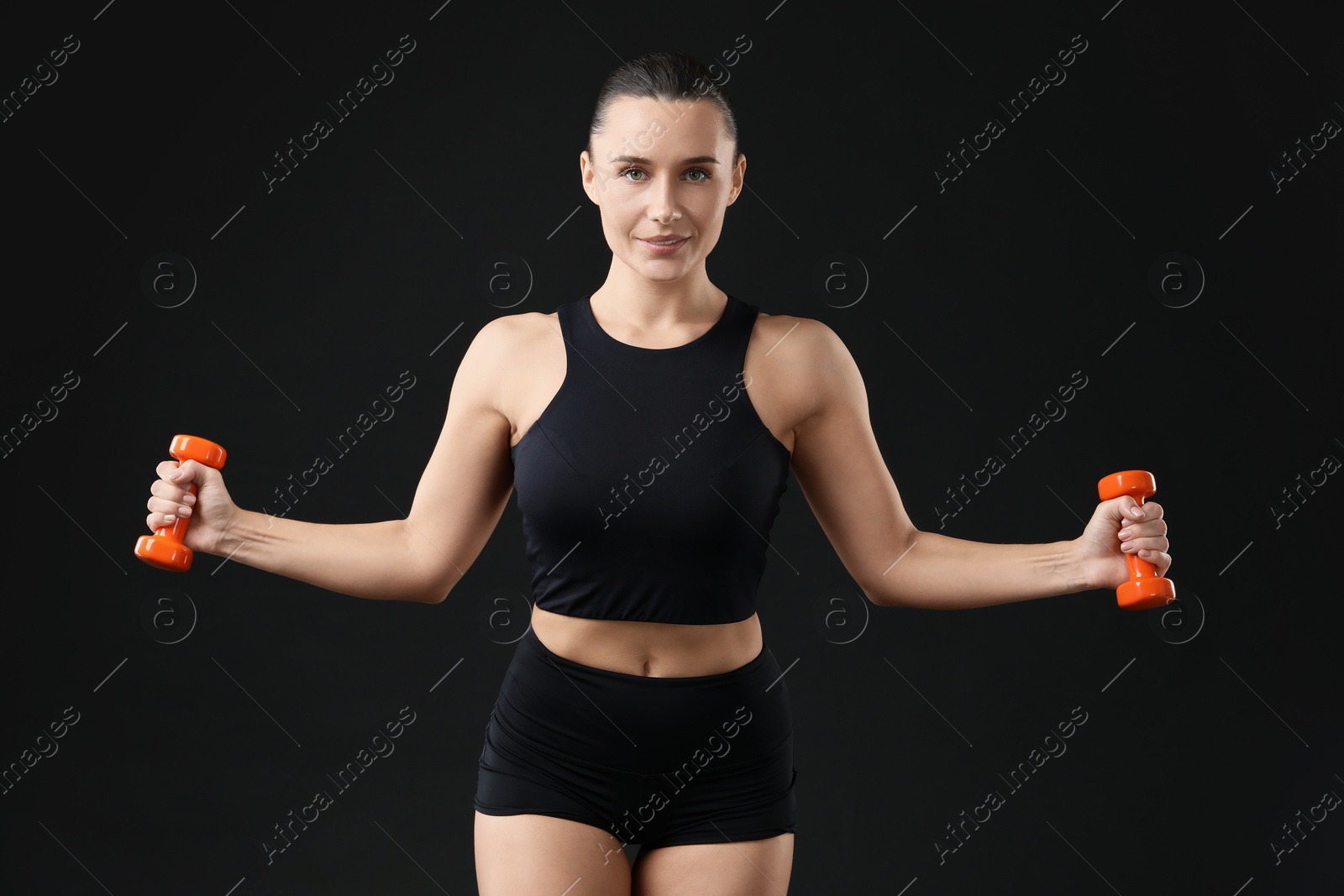 Photo of Woman exercising with dumbbells on black background