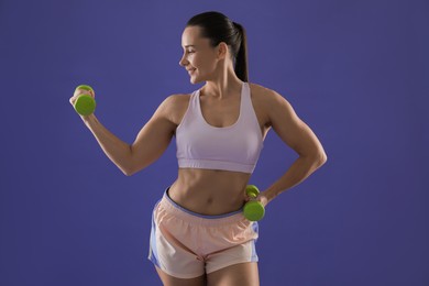 Woman exercising with dumbbells on purple background