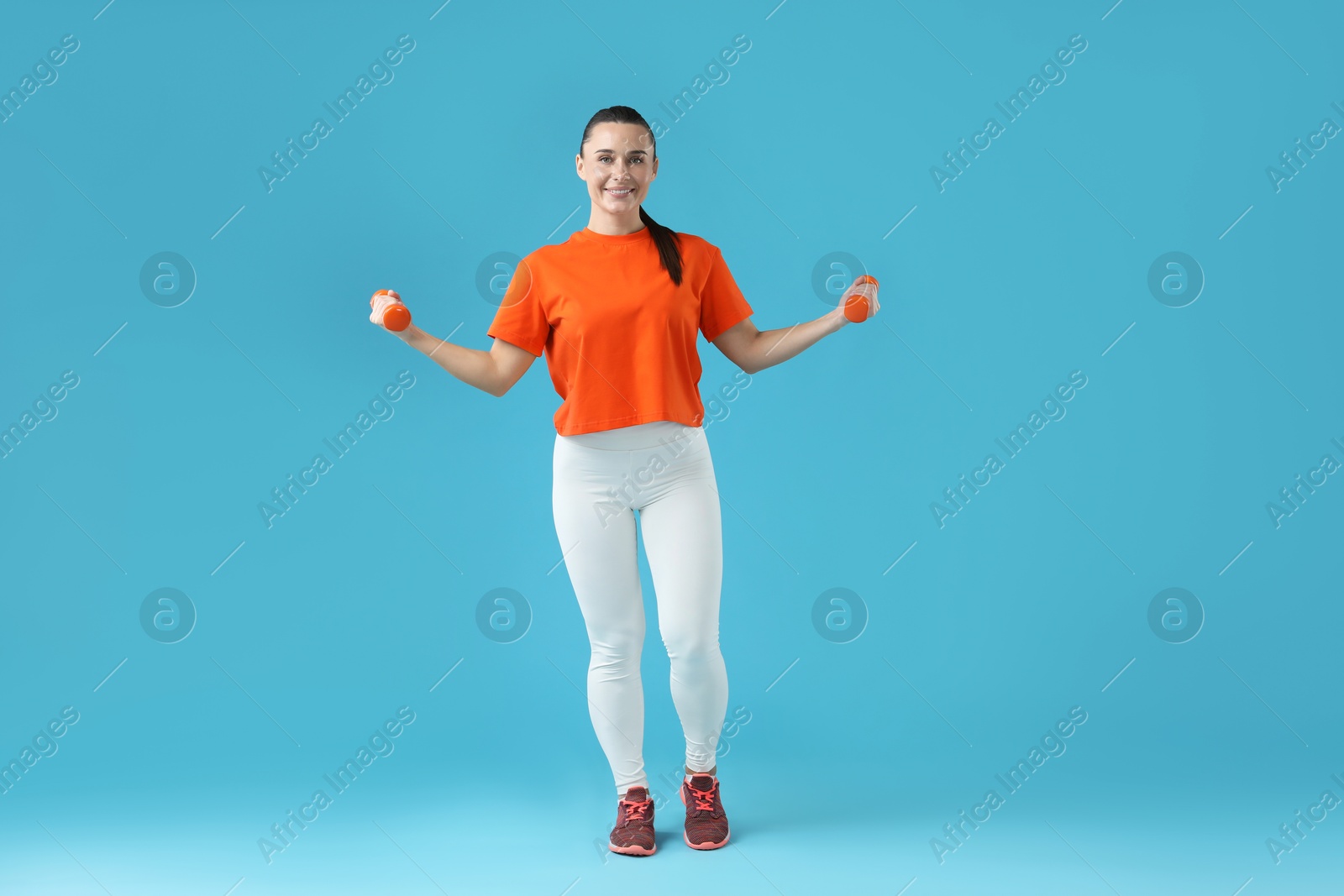 Photo of Woman exercising with dumbbells on light blue background