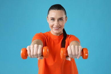 Photo of Woman exercising with dumbbells on light blue background