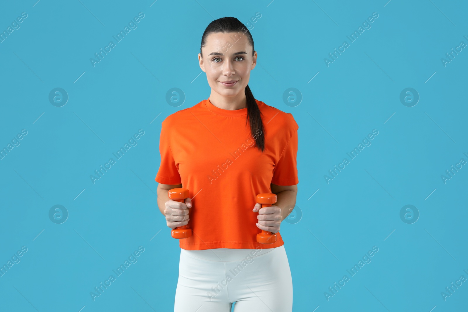 Photo of Woman exercising with dumbbells on light blue background