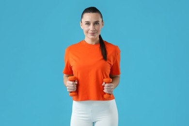 Photo of Woman exercising with dumbbells on light blue background