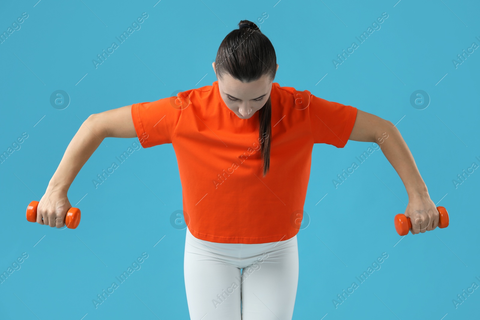 Photo of Woman exercising with dumbbells on light blue background