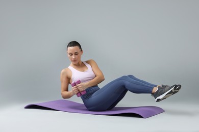 Photo of Woman exercising with dumbbells on fitness mat against light grey background