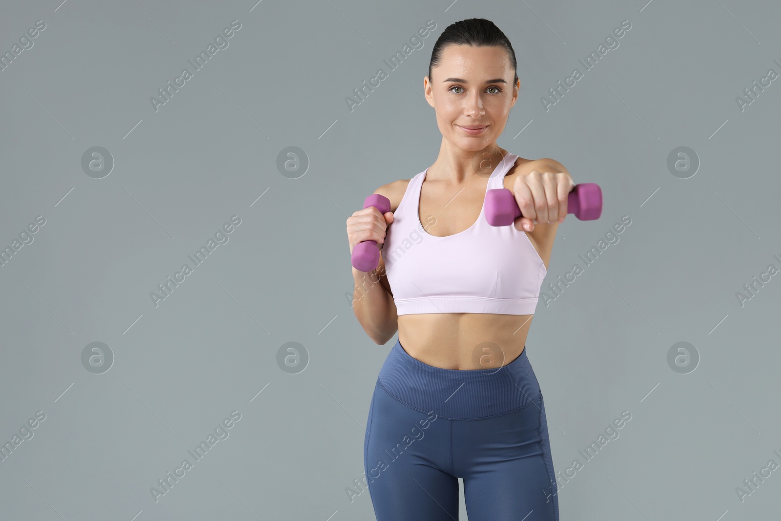 Photo of Woman exercising with dumbbells on light grey background, space for text