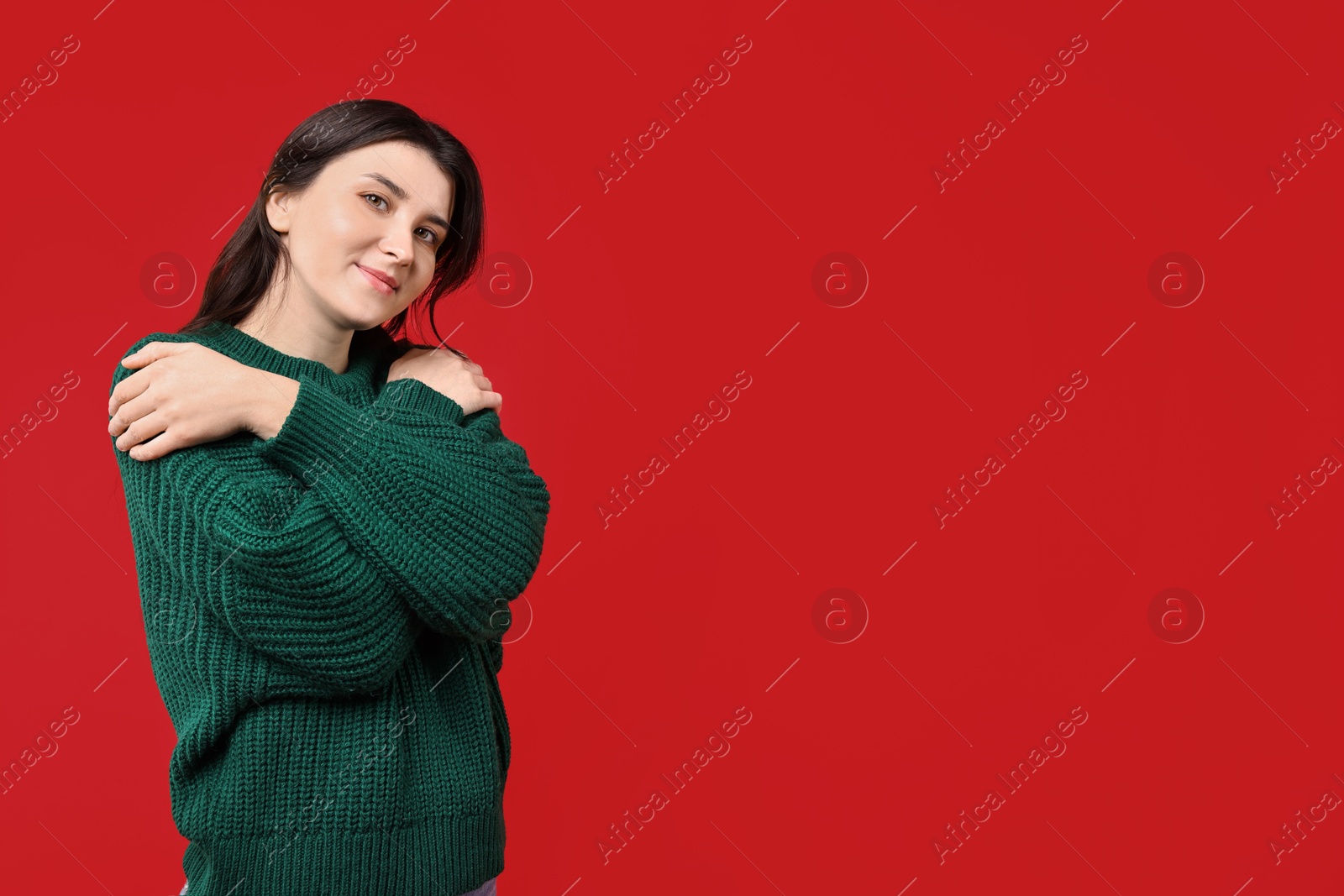 Photo of Beautiful young woman hugging herself on red background, space for text