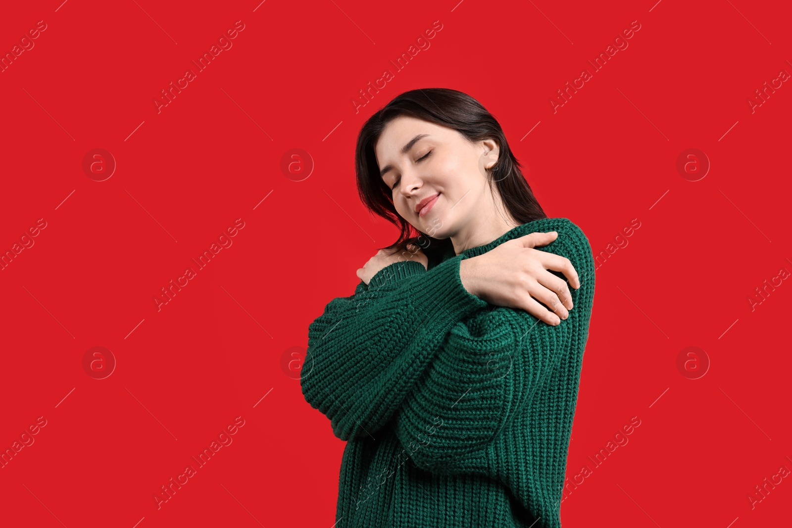 Photo of Beautiful young woman hugging herself on red background, space for text