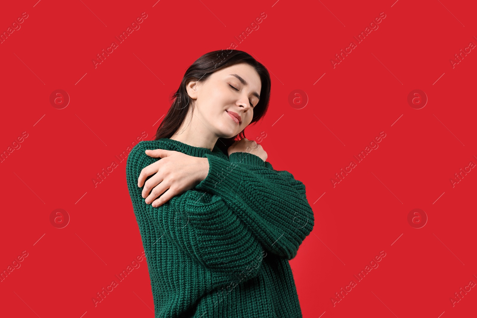 Photo of Beautiful young woman hugging herself on red background