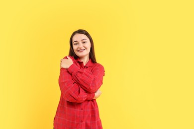 Photo of Beautiful young woman hugging herself on yellow background, space for text