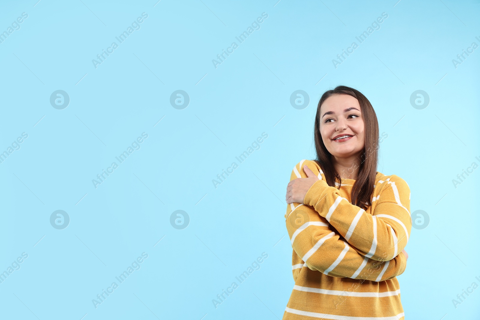 Photo of Beautiful young woman hugging herself on light blue background, space for text