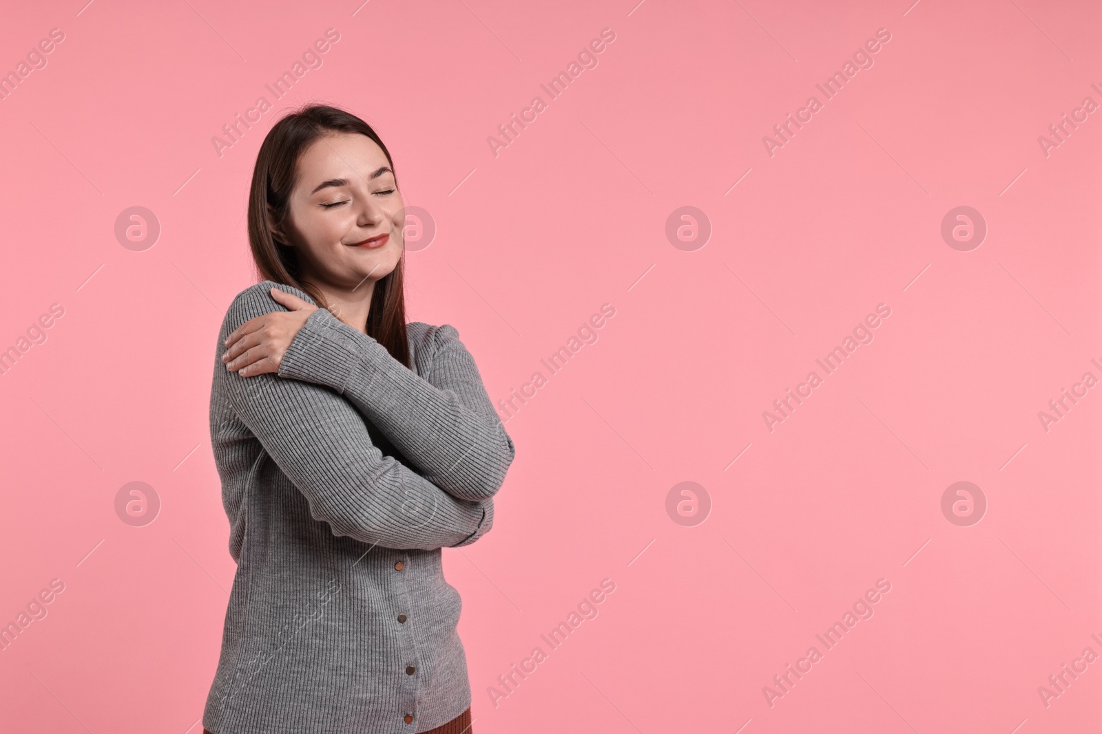 Photo of Beautiful young woman hugging herself on pink background, space for text