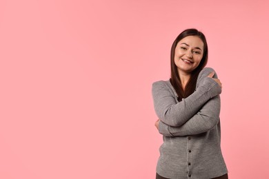 Photo of Beautiful young woman hugging herself on pink background, space for text