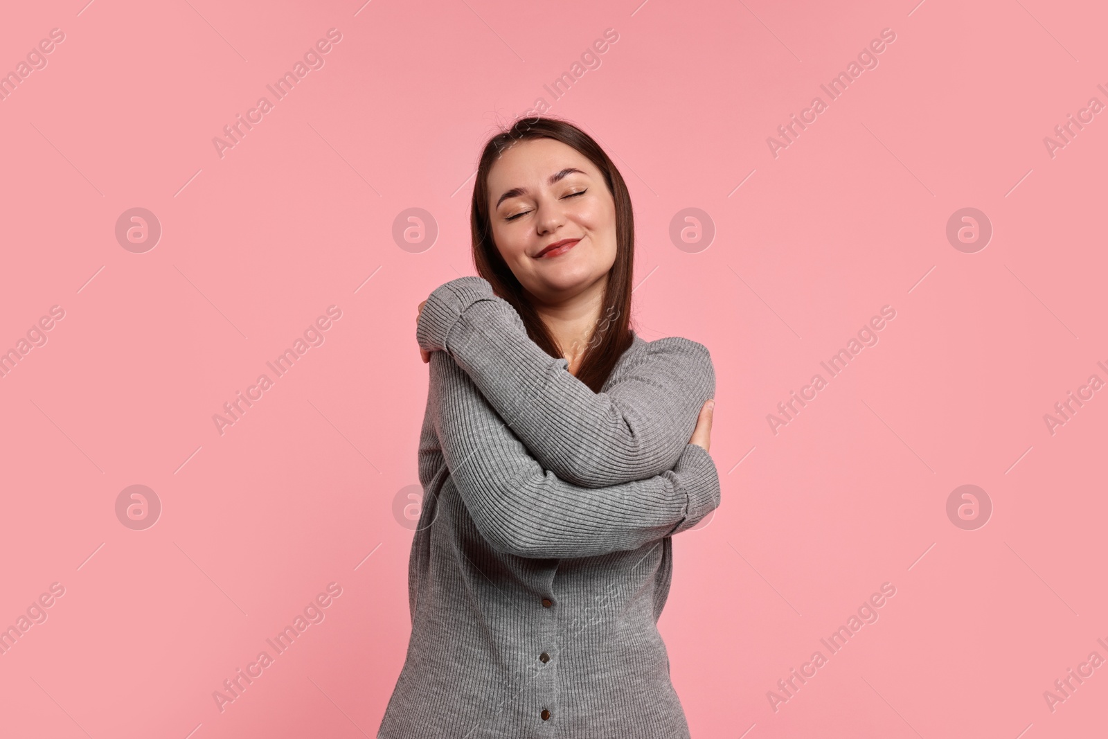 Photo of Beautiful young woman hugging herself on pink background