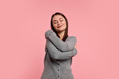 Photo of Beautiful young woman hugging herself on pink background