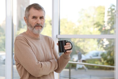 Photo of Mature man with cup of hot drink at home. Space for text