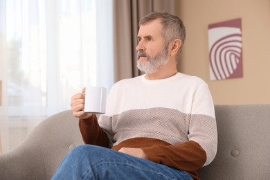 Photo of Mature man with cup of hot drink on sofa at home