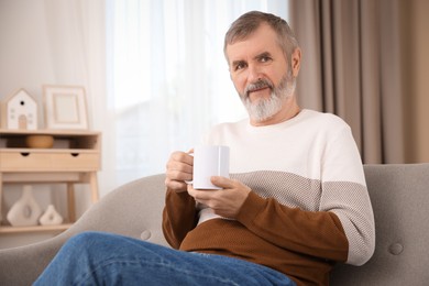 Photo of Mature man with cup of hot drink on sofa at home